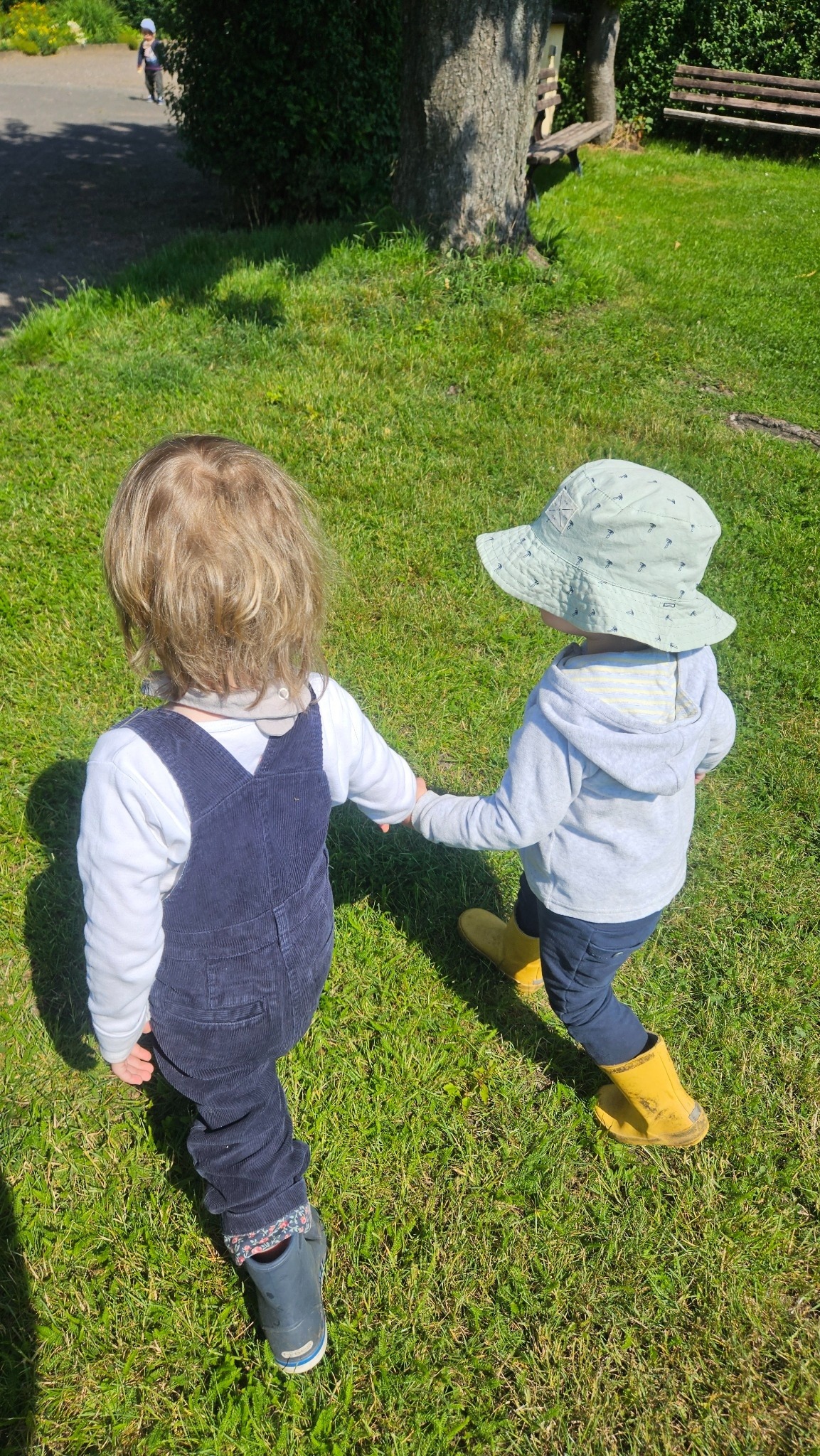 Zwei Kinder halten sich an der Hand im Park